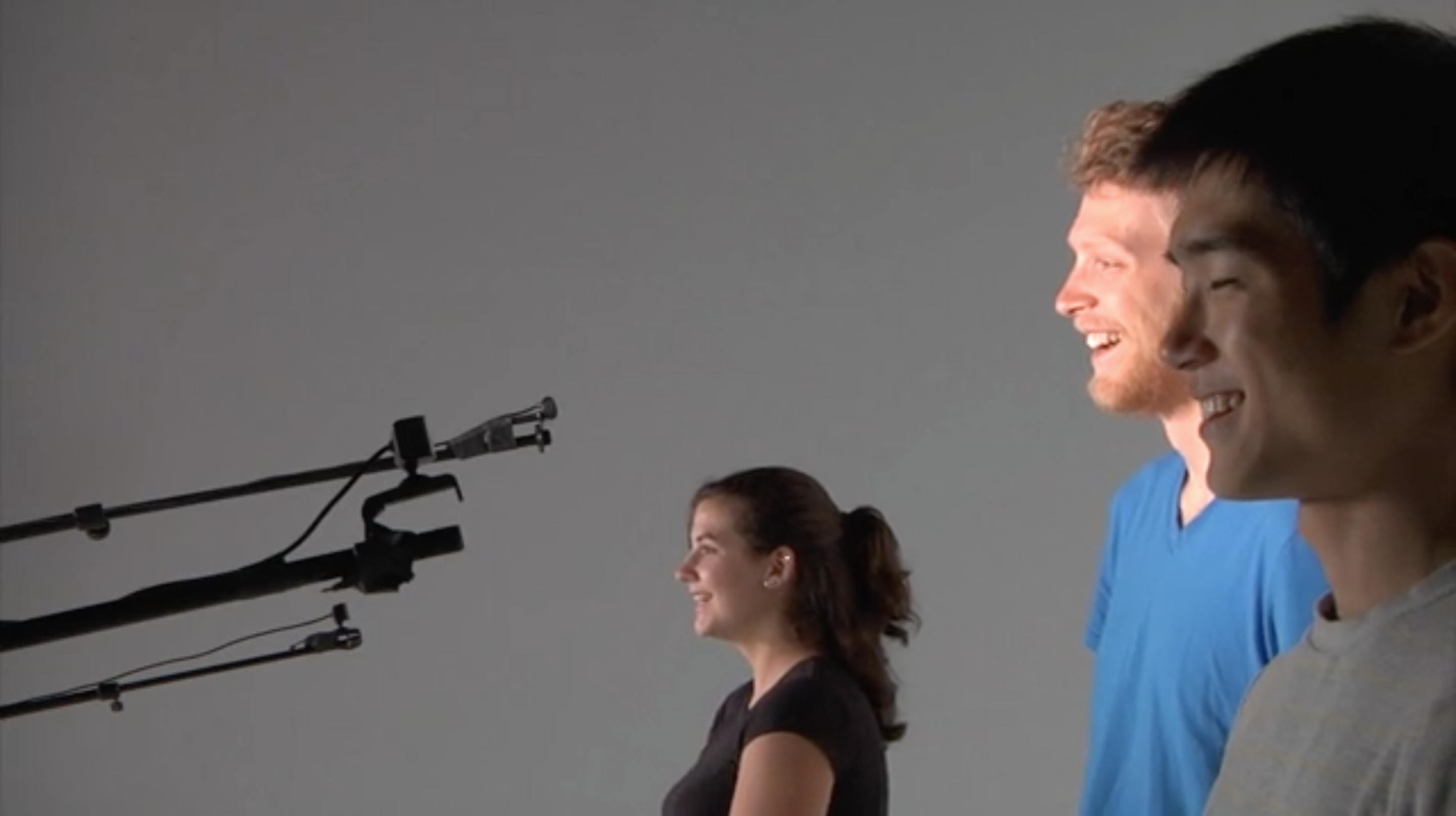 image of plink blink, an installation with three people standing in front of microphone stands with cameras on them, blinking to make music